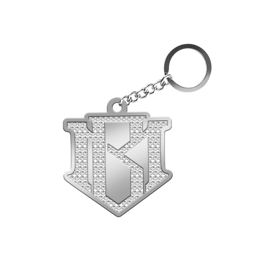 A silver-toned metal keychain featuring a shield-shaped pendant with a textured, rhinestone-embellished design and a polished central letter 'K', attached to a short chain and split ring on a plain white background.